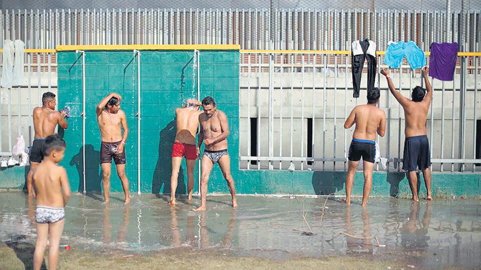 Cientos de inmigrantes centroamericanos se bañan en duchas en un improvisado campamento.