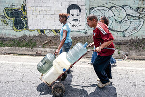 Un hombre empuja un carretilla con bidones cargados en un canal de aguas servidas en Caracas. (Fuente: AFP)