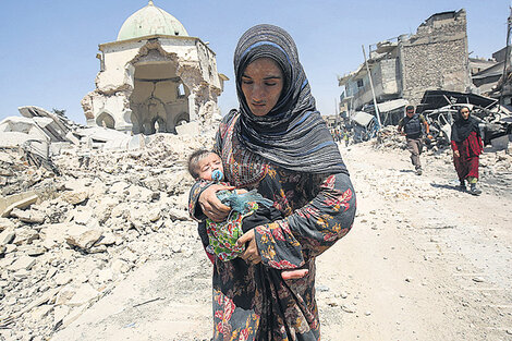 Una mujer camina con su bebé delante de las ruinas de mezquita de Al Nuri, en el oeste de Mosul.