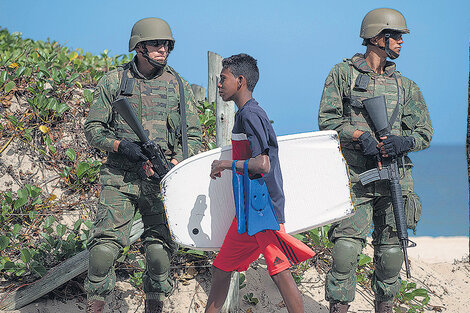 Un joven con tabla de barrenar pasa delante de un par de policías en la playa de Ipanema en Río de Janeiro. (Fuente: AFP)