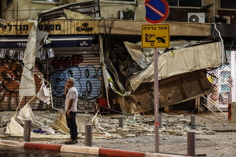 Un hombre se para frente a un negocio bombardeado en Tel Aviv.