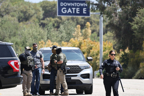 Una policía de Los Ángeles camina cerca de agentes federales enmascarados en la entrada del Dodger Stadium