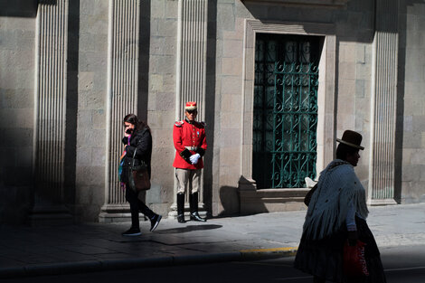 El palacio Quemado, un custodio y dos mujeres bolivianas: una con sombrero, otra con celular.