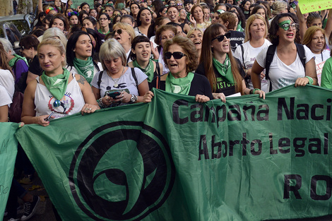 Mabel, con anteojos negros y pelo corto, al frente de la bandera de la Campaña por el Aborto Legal, Seguro y Gratuito.