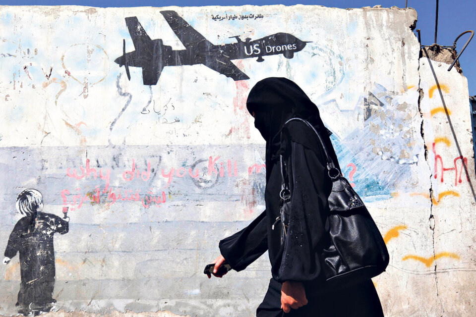 Una mujer yemení pasa al lado de un graffiti que condena las operaciones militares de EE.UU.