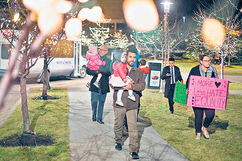 Una familia siria llega a Nebraska; la mujer lleva un cartel que dice : “Más amor, menos odio: igualdad”.