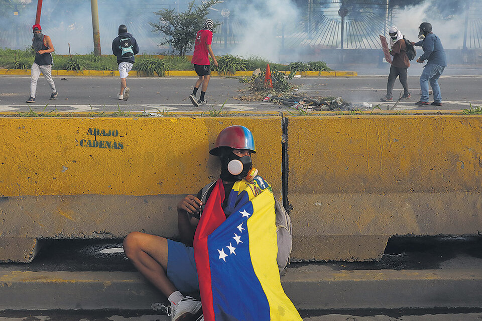 Un manifestante se protege detrás de un muro durante una protesta contra el gobierno de Maduro. (Fuente: EFE)