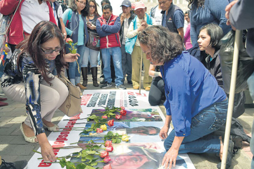 Amigos de las víctimas en Quito dejan flores en una bandera con las caras de los asesinados. (Fuente: AFP)