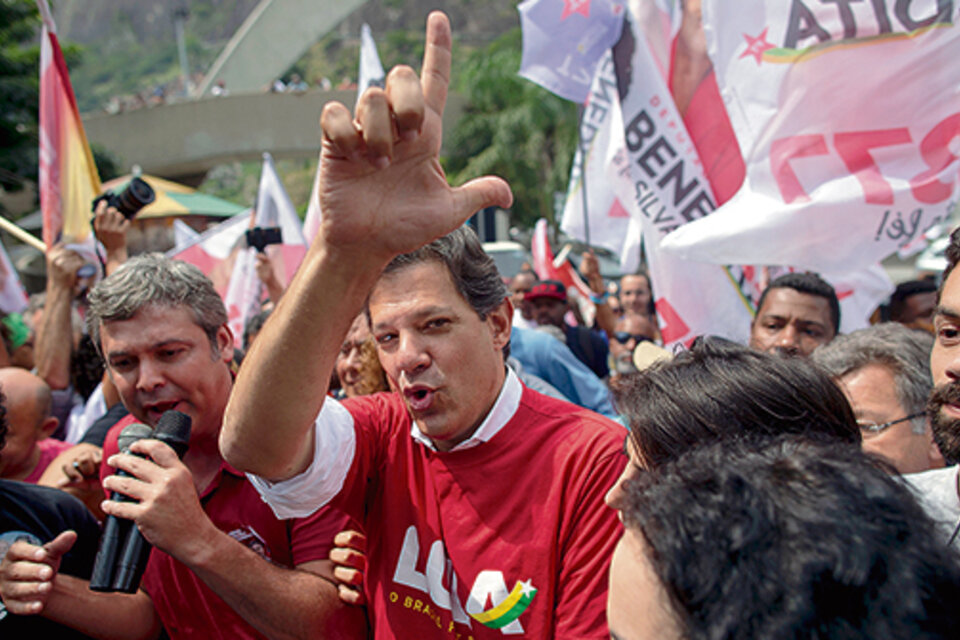 Rodeado por simpatizantes, Haddad hace la L de Lula con sus dedos durante su recorrida por Rocinha.