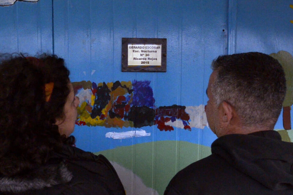 Ana Lucas y Adrián Gómez, docentes, frente a la placa que recuerda a Pichón en su escuela.