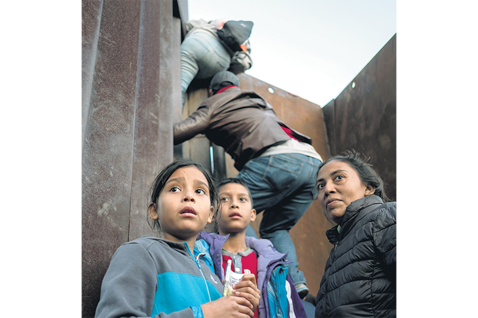 Niños de la caravana migrante trepan por una parte de la pared fronteriza. (Fuente: AFP)