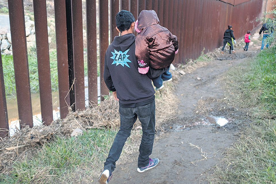 Un migrante con un niño en brazos camina en la frontera ente San Diego y Tijuana.