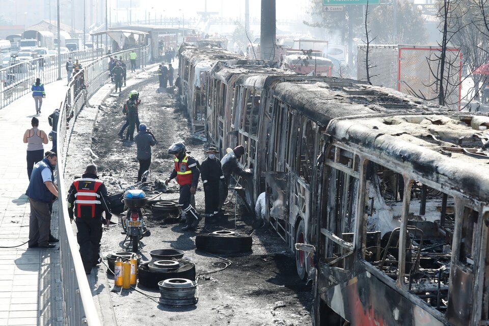 Funcionarios y peritos trabajan con los restos de buses de TransMilenio incinerados durante las protestas.  (Fuente: EFE)