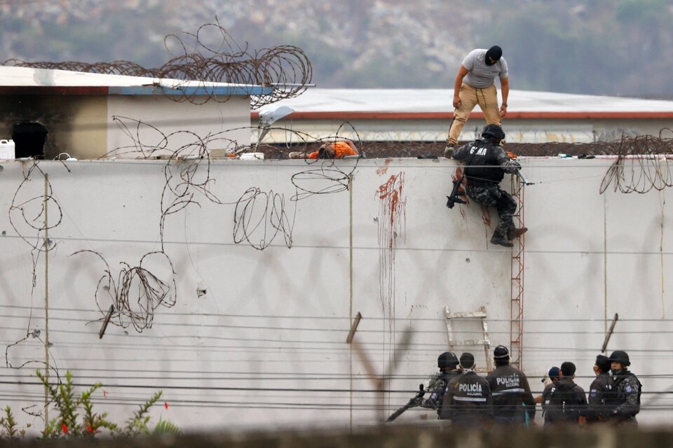 Policías ecuatorianos trepan un muro de la cárcel, donde yace el cuerpo de un recluso. (Fuente: AFP)