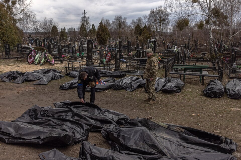 Dos policías observan los cadáveres trasladados al cementerio de Bucha.  (Fuente: EFE)