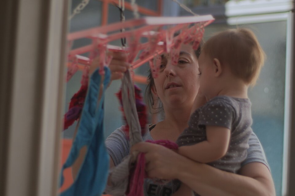 Colgar la ropa con un bebé en brazos, una imagen que de tan arquetípica esconde su esfuerzo. (Fuente: Gentileza serie Las Tareas)