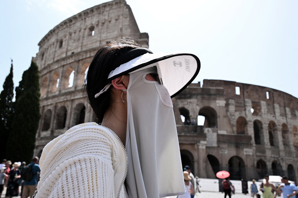 Una turista camina con ropa de protección solar frente al Coliseo.