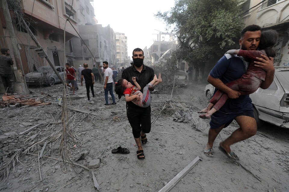 Dos hombres palestinos trasladan en brazos a niños heridos tras un ataque aéreo israelí.  (Fuente: EFE)