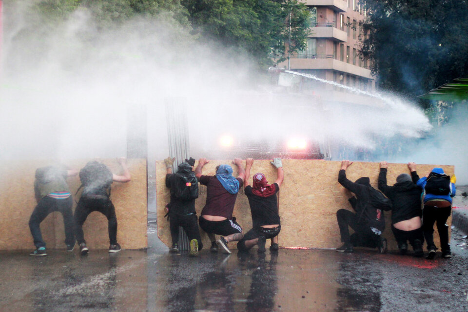 Resistiendo los chorros de los camiones hidrantes en las calles de Santiago. (Fuente: EFE)