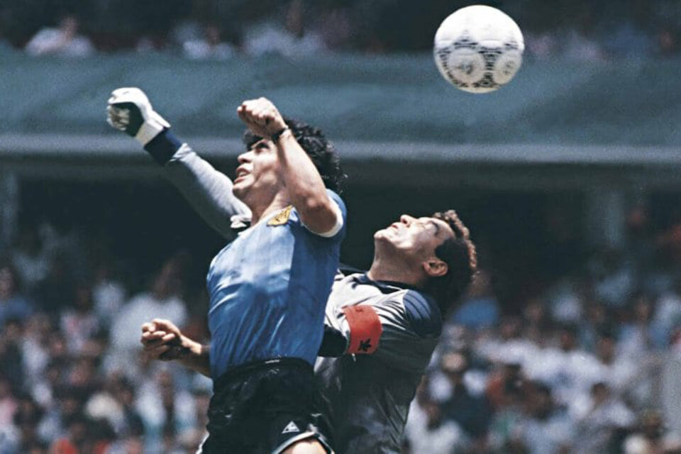 Maradona salta y empuja la pelota con la mano.