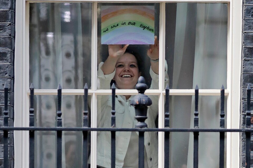 Una mujer muestra el arcoiris que se ve en las ventanas por estos días de encierro; este aparece desde la residencia oficial del primer ministro.  (Fuente: AFP)