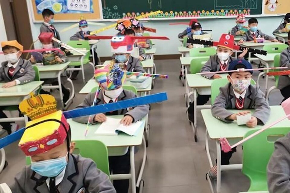Una escuela de Zheijiang, China, donde los niños usan sombreros de cartón, con varillas a los costados para el distanciamiento.
