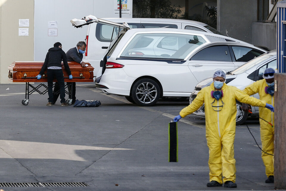 Empleados de una funeraria de Santiago cargan a un auto el cuerpo de un muerto por coronavirus. (Fuente: AFP)
