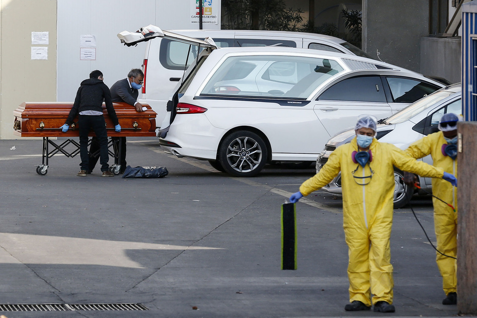 Empleados de una funeraria de Santiago cargan a un auto el cuerpo de un muerto por coronavirus.