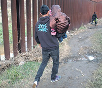 Un migrante con un niño en brazos camina en la frontera ente San Diego y Tijuana.