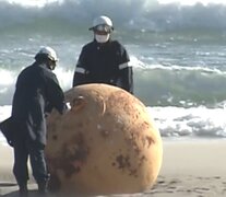 Dos agentes del escuadrón antibombas analizan la esfera de metal encontrada en la playa japonesa de Enshuhama. (Foto: captura de pantalla NHK)