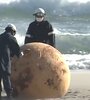 Dos agentes del escuadrón antibombas analizan la esfera de metal encontrada en la playa japonesa de Enshuhama. (Foto: captura de pantalla NHK)